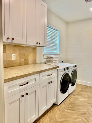 A laundry room with a stacked washer and dryer, beige tiled backsplash, and white cabinetry. - Inviting Gateway Near Galveston Beach for families,friends,business travelers. (La Marque)