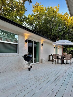 Eine Terrasse mit Grill, Gartenmöbeln und einem Sonnenschirm.
