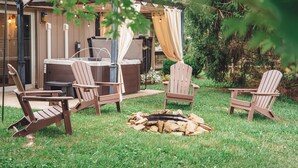 Ein Außenbereich mit Adirondack-Stühlen, einer Whirlpool-Badewanne und einer Feuerstelle.