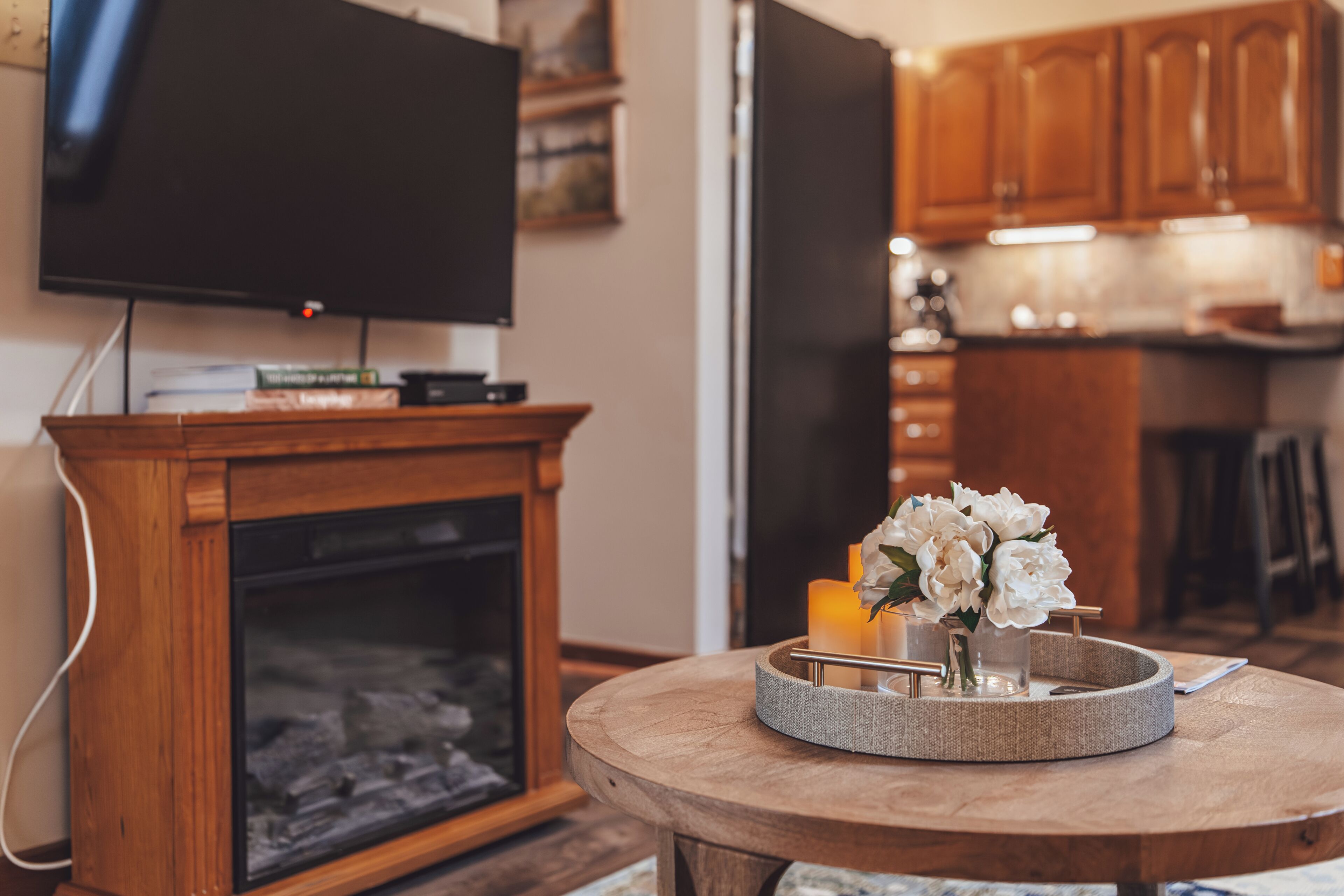 A living room with a fireplace, a television on a stand, and a round table with a candle and flowers.