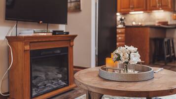A living room with a fireplace, a television on a stand, and a round table with a candle and flowers.