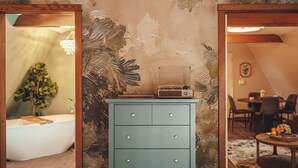 Ein Zimmer mit einem salbeigrünen Schminktisch, einer Badewanne und einem Essbereich mit Stühlen und einem Tisch.