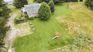 Une propriété résidentielle dotée d’une pelouse bien entretenue, d’une structure de jeu en bois et d’un grand arbre.