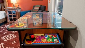 Quarto com mesa de vidro, cama, cadeira, abajur e parede com quadros.