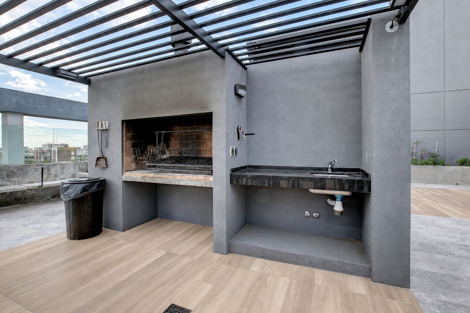 An outdoor kitchen area with a grill, sink, and trash can.