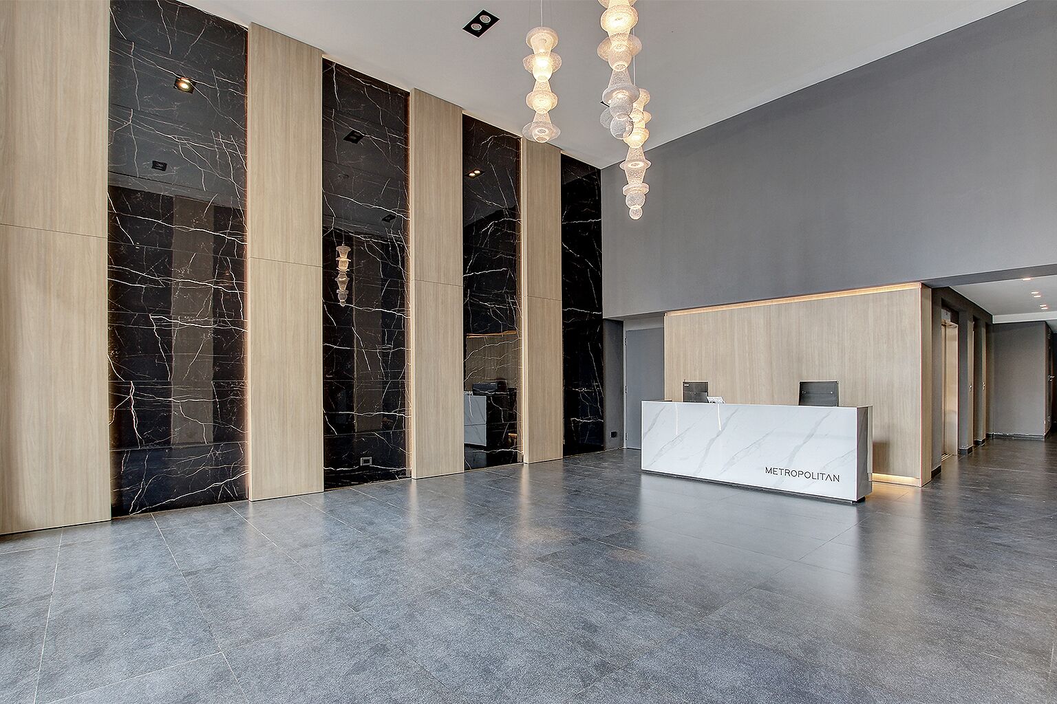 A modern reception area with a marble reception desk, wooden paneling, and pendant lighting.
