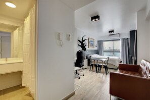 Ein Hotelzimmer mit Bett, Schreibtisch mit Stuhl, Badezimmer mit Spiegel und Fenster mit Vorhängen.