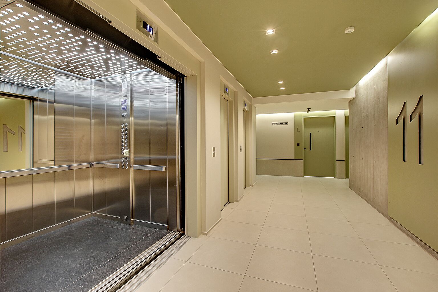 A modern elevator with a metallic finish and a control panel, leading to a hallway with a tiled floor and a door marked with the number 11.