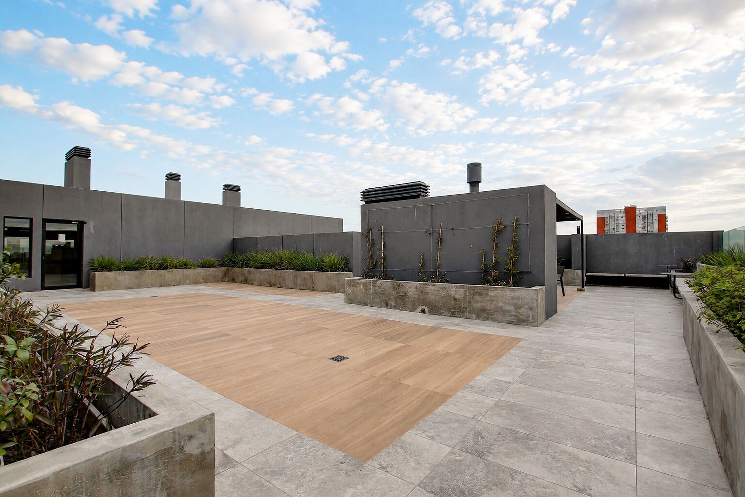 A rooftop terrace with a wooden deck, concrete walls, and a clear sky.