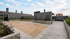 Terraço no topo do prédio com deck de madeira, paredes de concreto e céu claro.