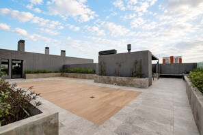 Eine Dachterrasse mit Holzboden, Betonmauern und blauem Himmel.