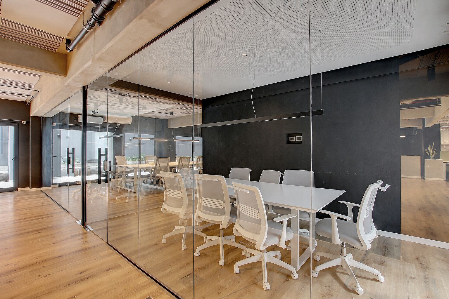 A modern conference room with glass walls, white chairs, and a black accent wall.