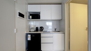 Cozinha compacta com armários brancos, micro-ondas, cafeteira e máquina de lavar louça.