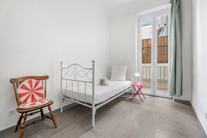 A bedroom with a bed, a chair, a small table, and a window with a view of the outside. - Appartement Le Verdi avec balcon  - Welkeys (Nice)