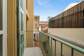 A narrow stairway with a green railing, leading to a building with a beige facade and a brown wall with a metal fence. - Appartement Le Verdi avec balcon  - Welkeys (Nice)