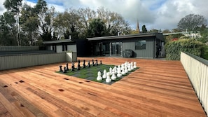 Un jeu d’échecs installé sur une terrasse en bois, avec un bâtiment moderne en arrière-plan.