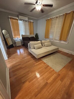 A room with a ceiling fan, a bed, a sofa, a mirror, and a window with curtains. - Modern Studio Near Toyota Center, Downtown Houston (Houston)