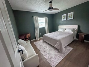 A bedroom with a bed, a chair, a small table, a ceiling fan, and a window with curtains. - Tranquil 3-bedroom house in sunny Sarasota (Sarasota)
