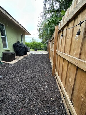 A backyard with a wooden fence, a covered patio table, and a black tarp.