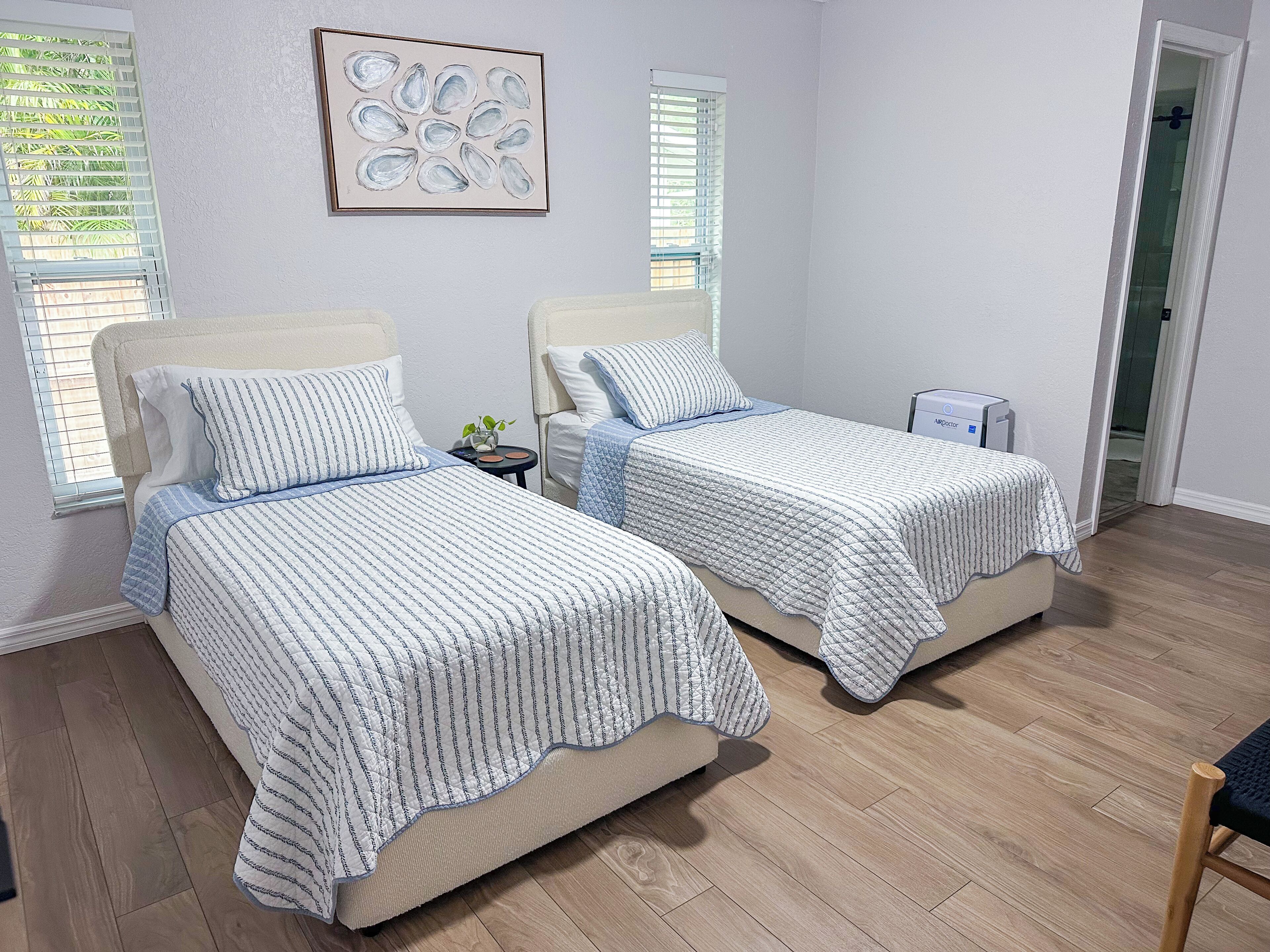 A bedroom with two beds, a small table, and a wall-mounted artwork.