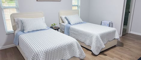 A bedroom with two beds, a small table, and a wall-mounted artwork.