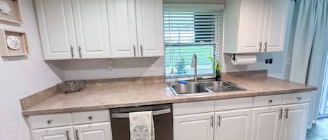 A kitchen with white cabinets, a stainless steel sink, a dishwasher, and a window with blinds.