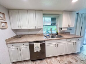A kitchen with white cabinets, a stainless steel sink, a dishwasher, and a window with blinds. - Tranquil 3-bedroom house in sunny Sarasota (Sarasota)