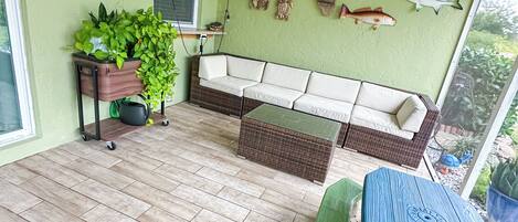 A room with a ceiling fan, a white sofa, a green bench, a blue table, and a wall with fish decorations.