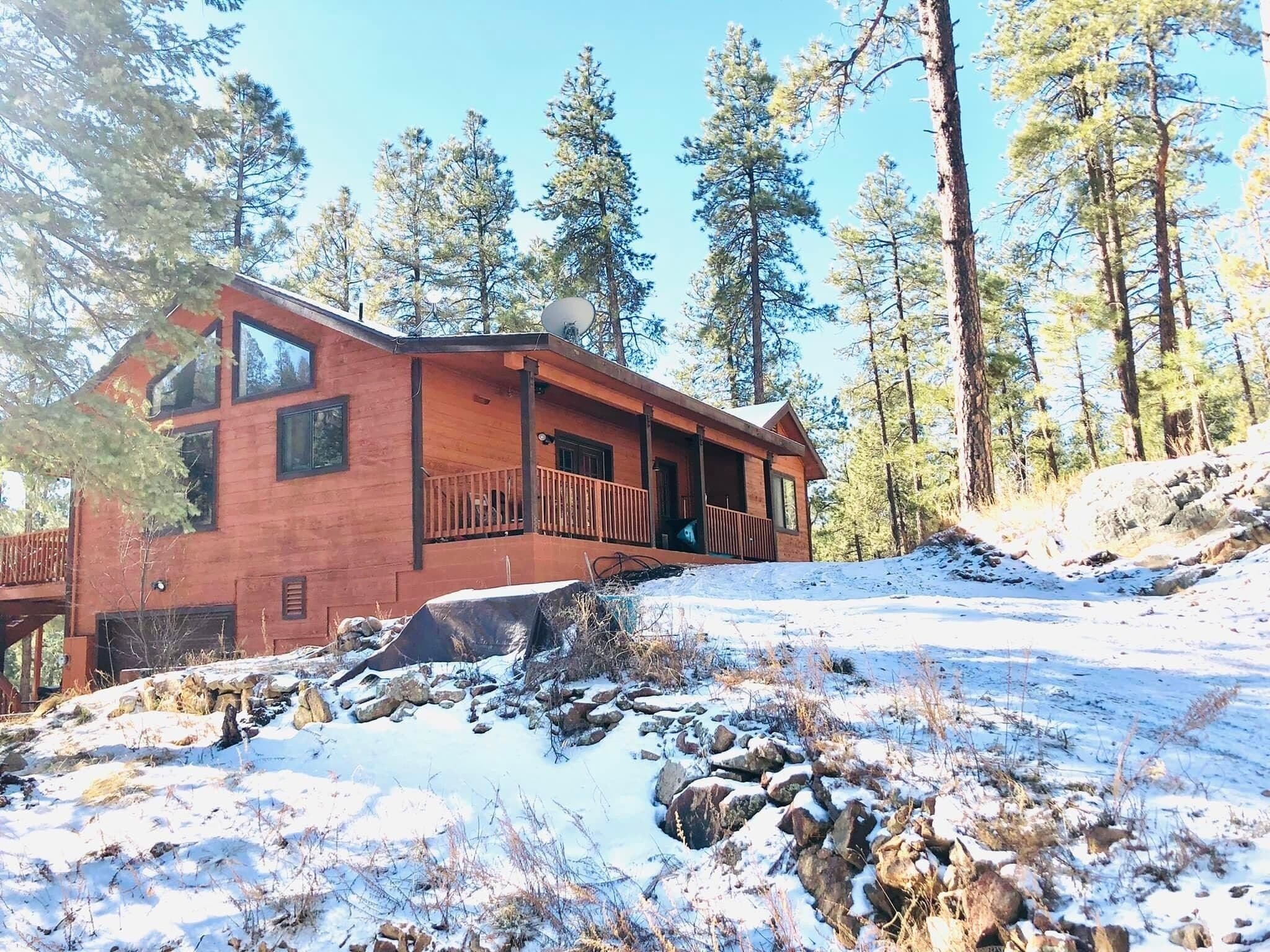 A wooden cabin with a balcony, surrounded by trees and snow.