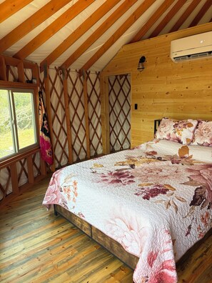 A bedroom with a wooden ceiling, a bed with floral bedding, a window, and a door with a lattice design.
