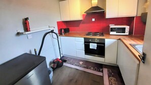 A compact kitchen with white cabinets, a red backsplash, a microwave, and a gas stove. - Joydens Wood, 2-Bed Apt, Sleeps 4 with Parking (Essex)