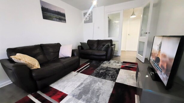A living room with two black sofas, a patterned rug, and a flat-screen TV. - Joydens Wood, 2-Bed Apt, Sleeps 4 with Parking (Essex)