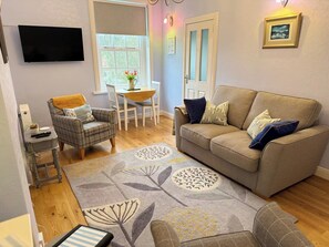 A living room with a sofa, armchair, and a dining table with chairs. - Largo Bay - Harbour Hideaway (Leven)