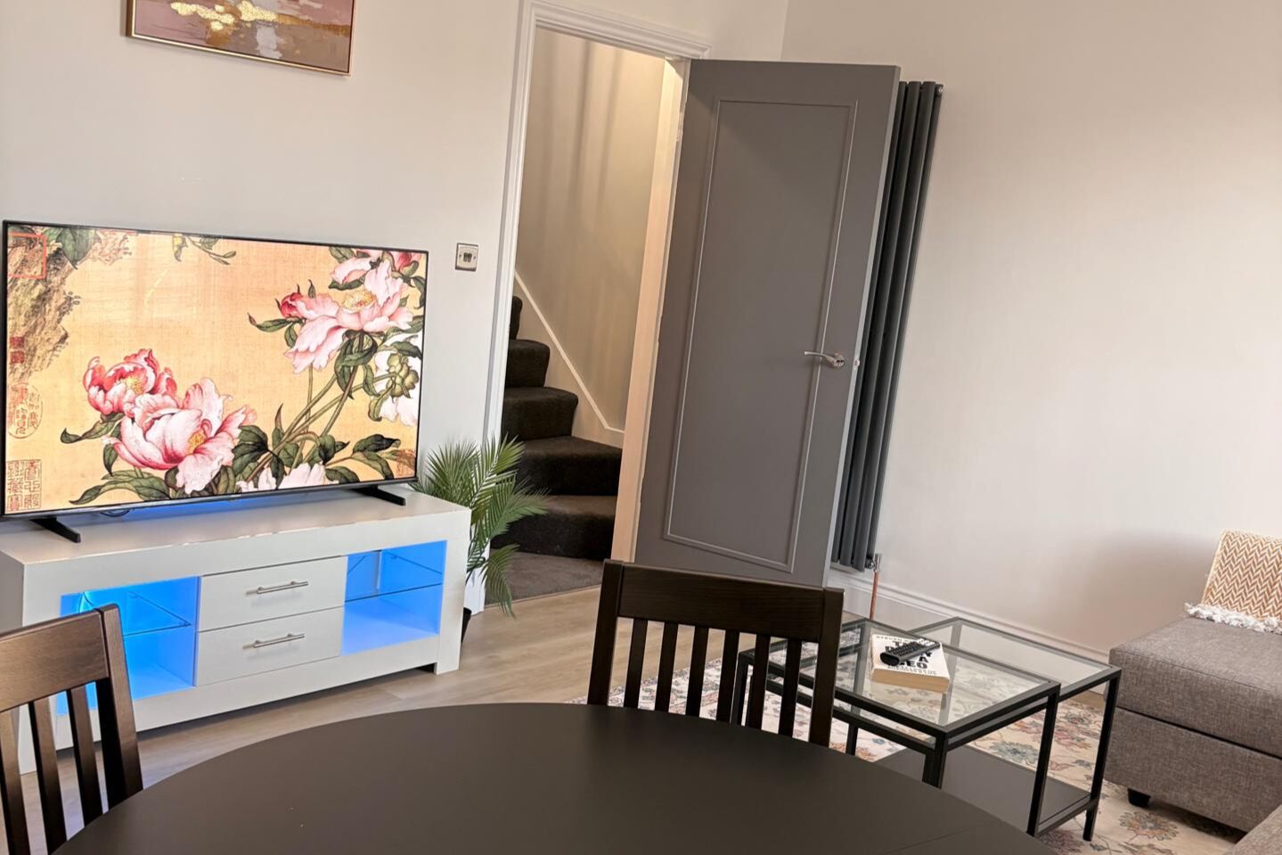 A living room with a flat-screen TV, a dining table, a sofa, and a staircase.