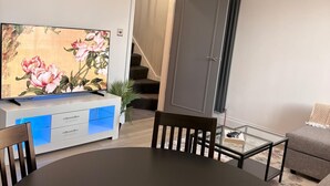 Uma sala de estar com televisão de tela plana, mesa de jantar, sofá e escada.