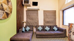 A room with a brown sofa set, a television mounted on the wall, and a patterned floor. - Collection O Lake Mall Kalighat (Kolkata)