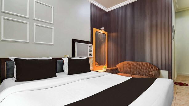 A hotel room with a large bed, a chair, a mirror, and a wall-mounted air conditioning unit. - Collection O Lake Mall Kalighat (Kolkata)