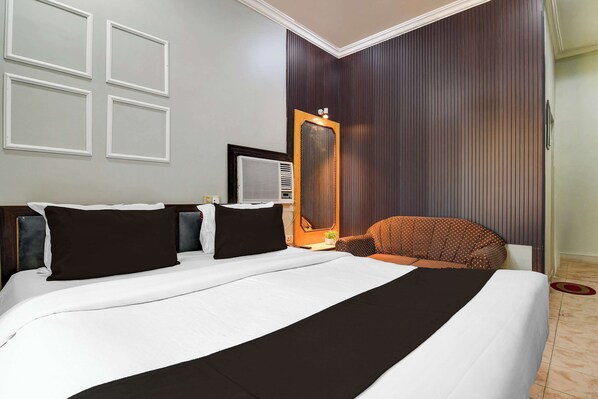 A hotel room with a large bed, a chair, a mirror, and a wall-mounted air conditioning unit.