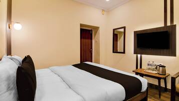 Habitación de hotel con cama, televisor montado en la pared, una mesita con hervidor y botellas de agua, y una puerta que da a otra habitación.