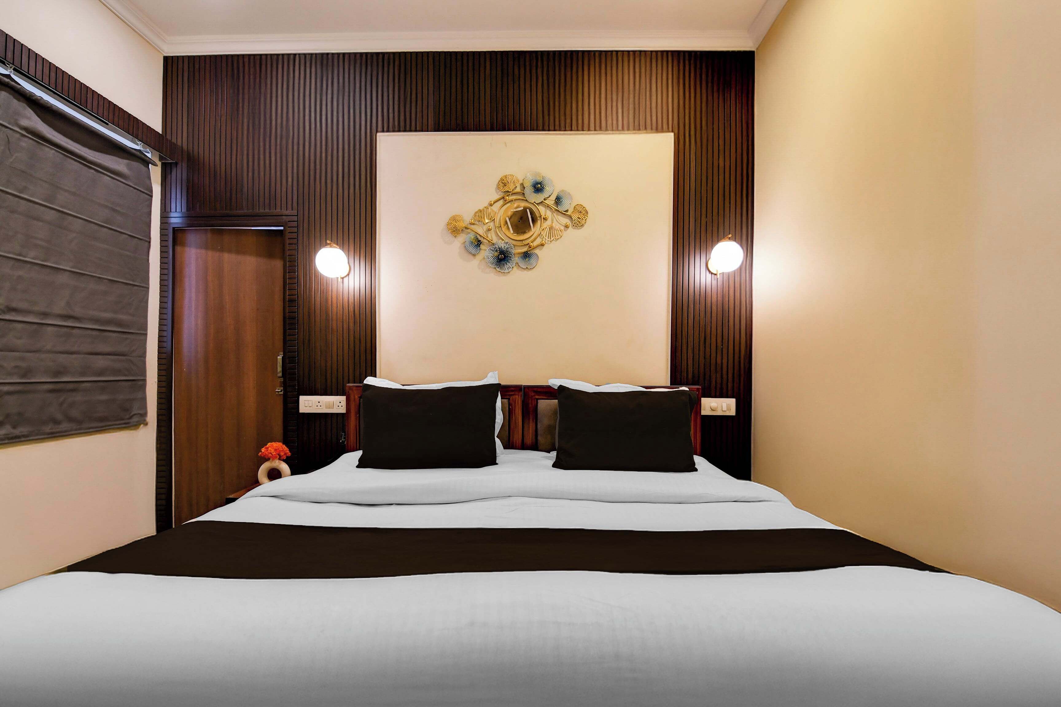A hotel room with a large bed, two bedside tables, a wall-mounted light fixture, and a decorative wall piece.