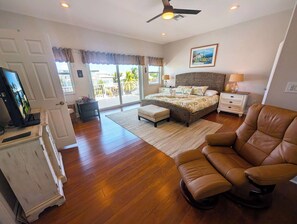 A bedroom with a bed, a chair, a television, and a view of the outdoors. - Beautiful Home in Port Antigua with Dock and Private Beach Access (Islamorada)