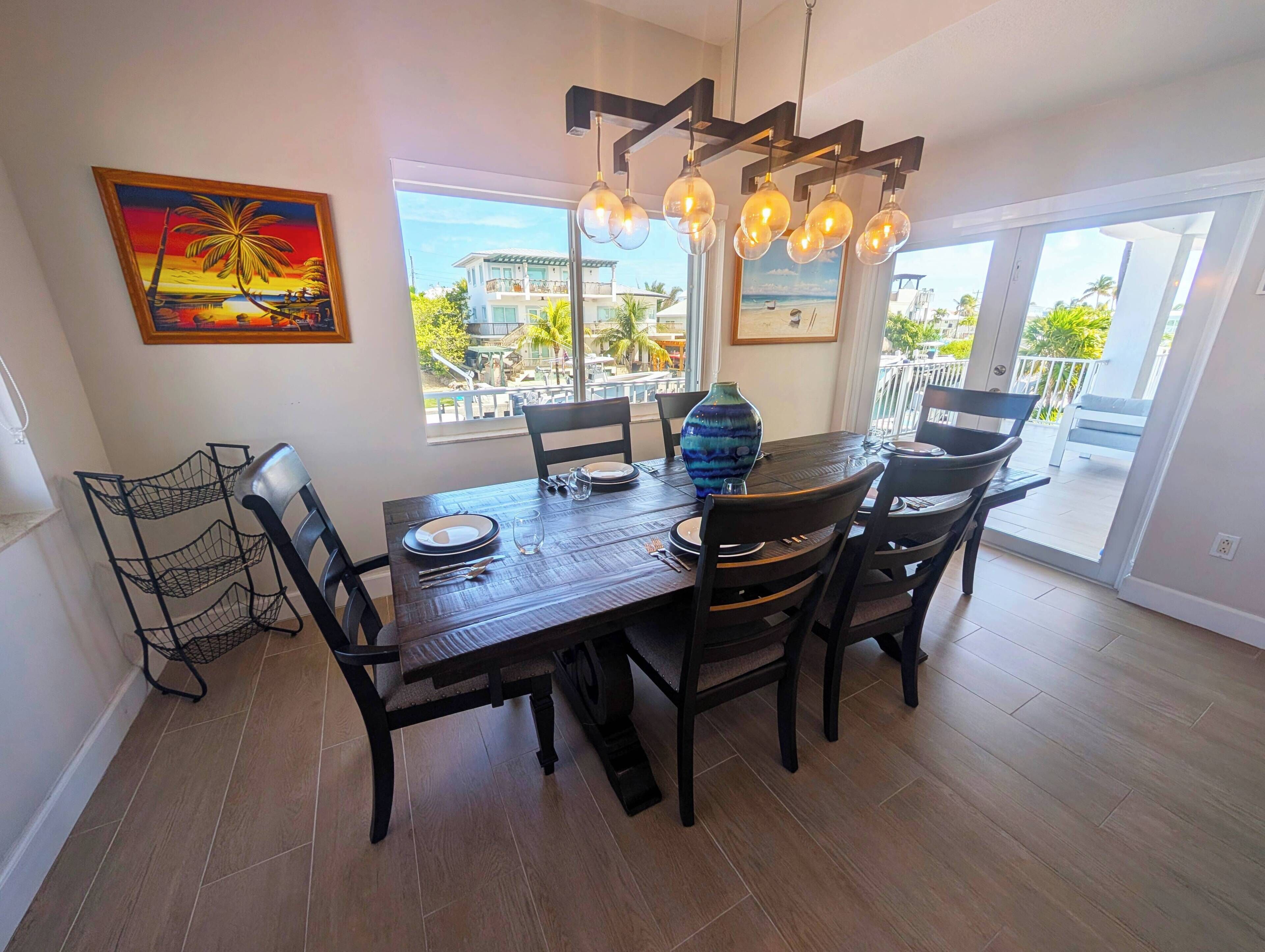 A dining area with a wooden table set for four, a large vase, and a painting on the wall.
