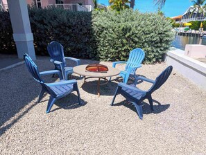A patio with four blue Adirondack chairs around a round table with a fire pit. - Beautiful Home in Port Antigua with Dock and Private Beach Access (Islamorada)