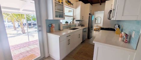 Moderni keittiö, jossa on valkoiset kaapit, ruostumattomasta teräksestä valmistettu jääkaappi ja laatoitettu välitila.