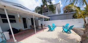 A covered outdoor area with a patio, two blue Adirondack chairs, and a white refrigerator. - Luxury Waterfront Retreat located in Tavernier, FL (Tavernier)