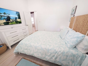 Ein Schlafzimmer mit einem Bett, einer Kommode, einem Fernseher und einer Tür zu einem anderen Raum.