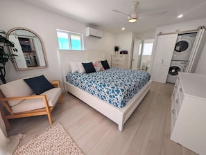 Ein Schlafzimmer mit Bett, Sessel, Kleiderschrank, Klimaanlage und Waschmaschine.