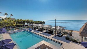 A pool area with a view of the sea, lounge chairs, umbrellas, and a thatched-roof structure. - Waterfront 2BR, 2BA Islamorada retreat with pool, hot tub, and kayaks. (Islamorada)