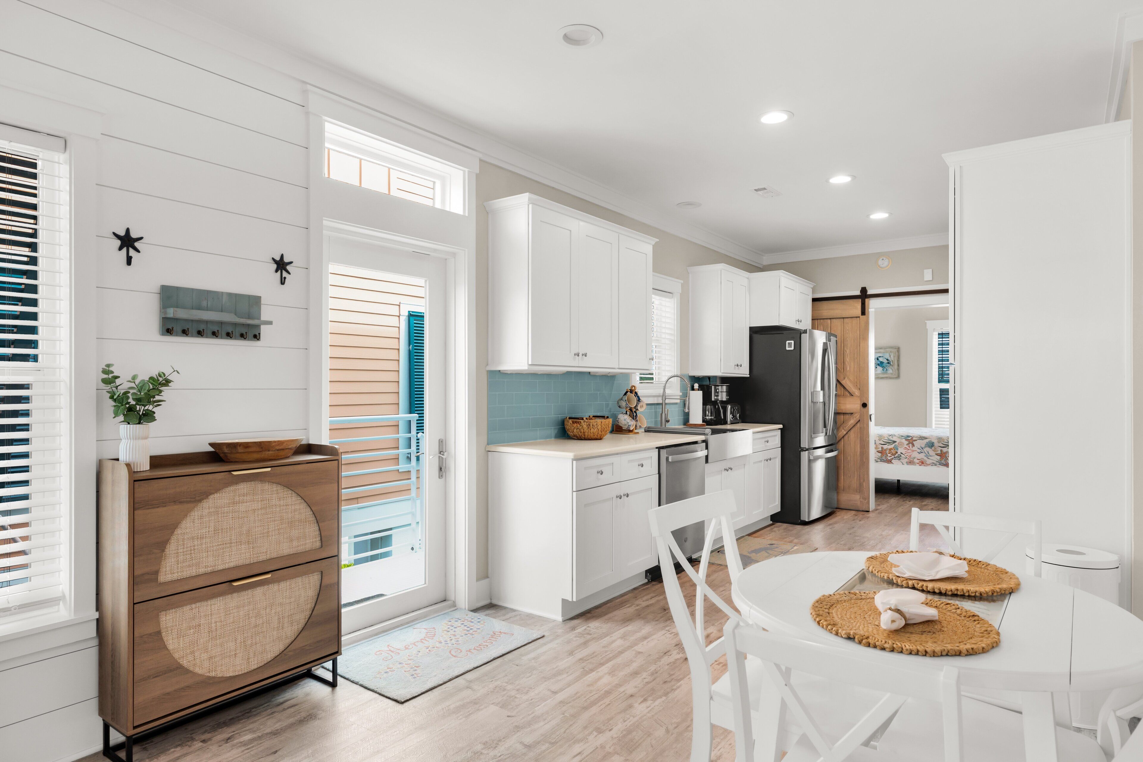 A modern kitchen with white cabinetry, a central island, and a dining area with a white table and chairs.