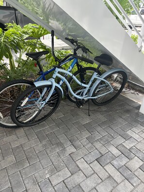 Two bicycles parked on a paved surface with a white wall and greenery in the background. - Waterfront 2BR, 2BA Islamorada retreat with pool, hot tub, and kayaks. (Islamorada)